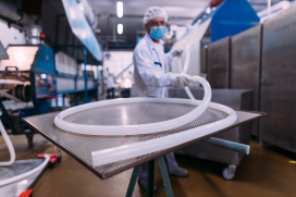 plastic tubing coiled on a metal sheet in a laboratory with a person in full medical PPE holding the end of the tube in the background