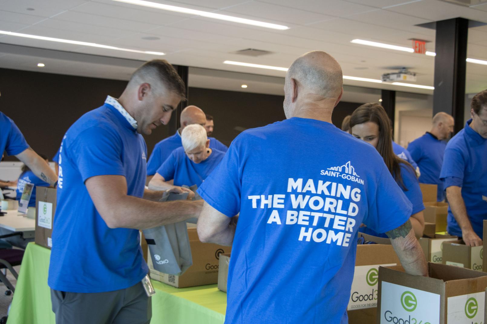 People wearing shirts that say "Making The World A Better Home" packing kits from cardboard boxes with Good360 logos on them.