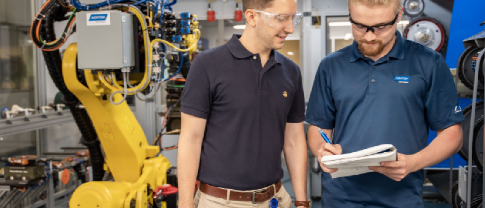 Two engineers at Saint-Gobain North America are discussing notes beside industrial robotic equipment, representing careers in the manufacturing industry.